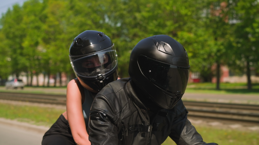 Young woman with helmet hugs boyfriend riding powerful motorcycle together along large city street on sunny spring day closeup slow motion