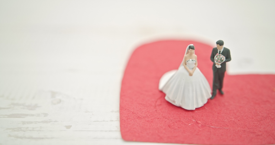 Wedding and eternal love concept : Miniature figurine couple wedding doll, bride and bridegroom with a bouquet stand on a red mulburry paper heart.