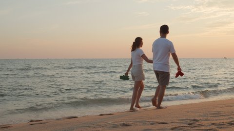 Vacation loving couple walking on beach together at sunset landscape, relaxing vacation travel summer, Asian man and woman in love holding hands walks along the sandy seashore