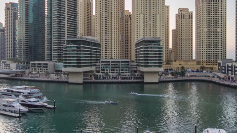 Dubai Marina waterfront with towers and yachts near restaurants from shoping mall balcony in Dubai day to night transition aerial timelapse, United Arab Emirates.