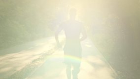 Healthcare and sporty lifestyle concept. Back view shot of young active muscular guy jogging in morning, running on path in green park, sun flare, slow motion