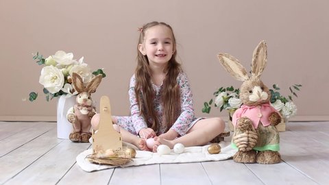Little girl playing with Easter toy bunnies and a basket of Easter eggs. Child celebrating Easter. Easter egg hunt. Home decoration, bunnies and flowers