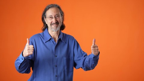 Promoter mature long hair bearded man 50s 60s orange shirt point fingers aside on workspace copy space mockup promo commercial area isolated on solid orange background studio portrait