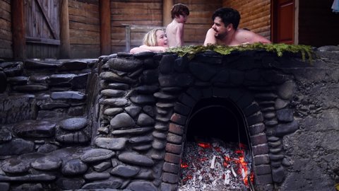 happy family with kids relaxing in hot bath tub outdoors, enjoying thermal spa in stone vat on fire. winter activity and leisure