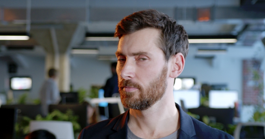 Close up of Caucasian handsome man looking at camera and smiling in office. Indoors. Portrait of young male with beard standing in coworking space. Successful leader and businessman. | Shutterstock HD Video #1089115795