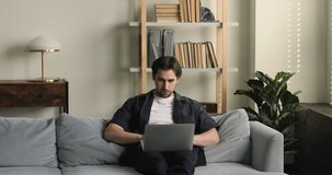 Relaxed millennial male rest on couch hold notebook chat with girlfriend in messenger enjoy virtual dating. Young man freelancer work from home create new project on laptop pc sitting on comfy sofa