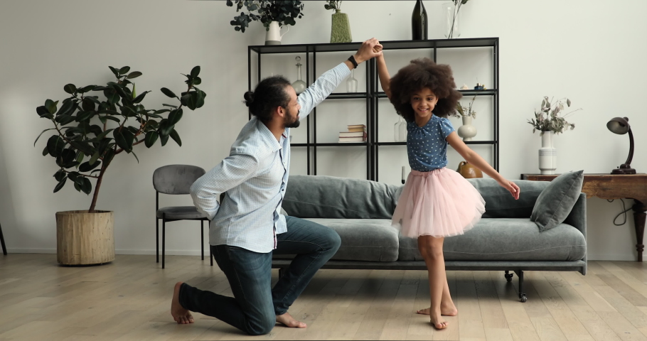 Caring Black dad stand on one knee hold hand of preteen daughter wearing fluffy skirt teach excited child to dance waltz. Father tween girl play princess knight dance on imaginary ball at living room Royalty-Free Stock Footage #1089117187