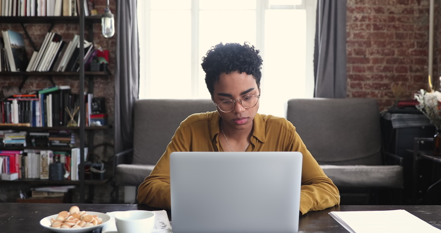 Serious young African lady study remote from home learn foreign language sit by laptop write down text translation using online virtual dictionary app. Teenage female in glasses prepare homework on pc Royalty-Free Stock Footage #1089117267