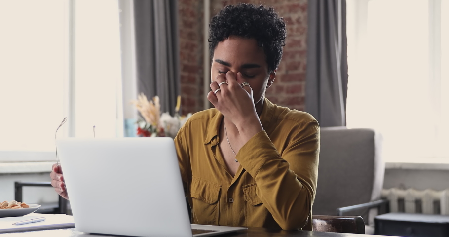 Tired young Black woman worker student take short pause in online work remove glasses massage nose bridge relax with closed eyes. Female employee overworked by pc feel fatigue suffer from eye strain | Shutterstock HD Video #1089117275