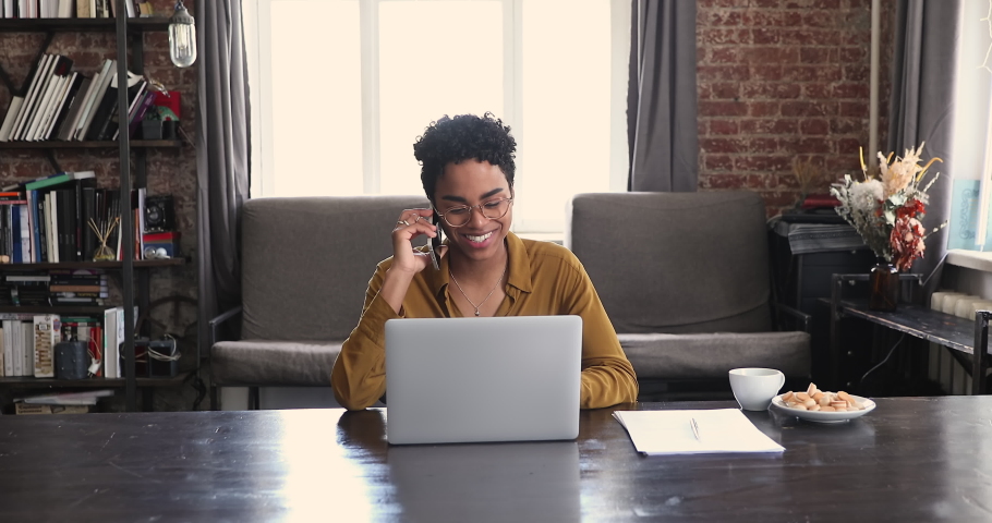 Young Black female hold phone conversation before laptop screen. Millennial African businesswoman sales manager discuss order detail with client by phone give advice make offer using computer database Royalty-Free Stock Footage #1089117331
