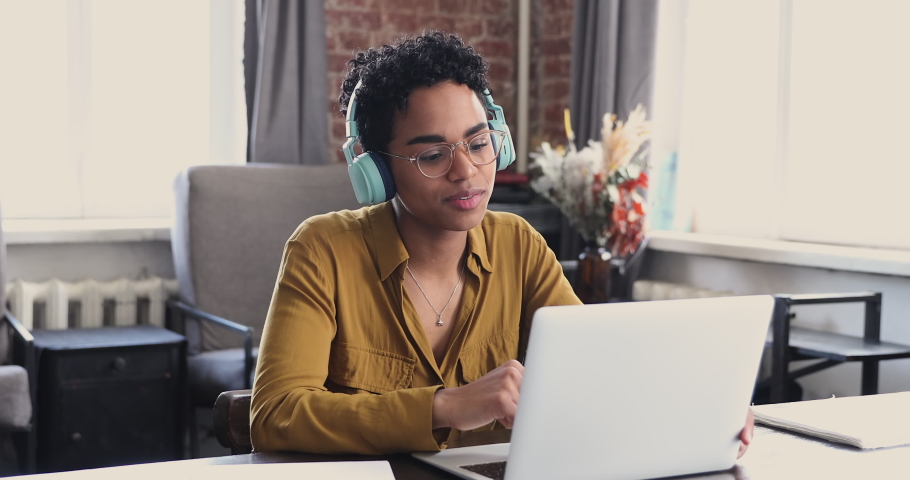 Young American female student employee in glasses wear earphones speak on webcam conference using app on laptop. Millennial lady remote worker talk by video call explain idea make offer to client Royalty-Free Stock Footage #1089117337