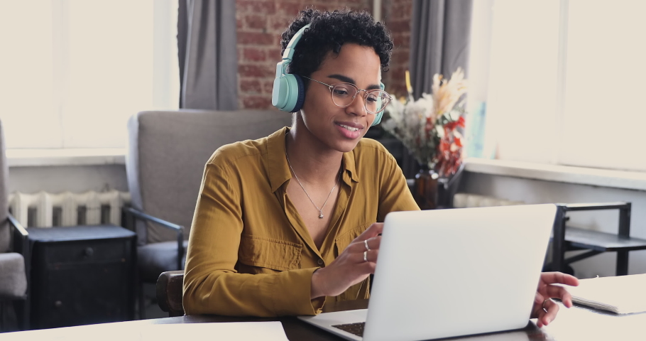 Young American female student employee in glasses wear earphones speak on webcam conference using app on laptop. Millennial lady remote worker talk by video call explain idea make offer to client Royalty-Free Stock Footage #1089117337