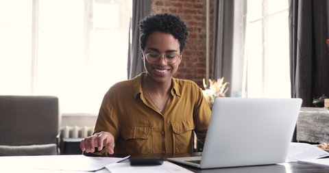 Young Black woman accountant use calculator to check sums in annual report smile satisfied with good result of budgeting work. Female entrepreneur calculate earnings expenses enjoy profitable business