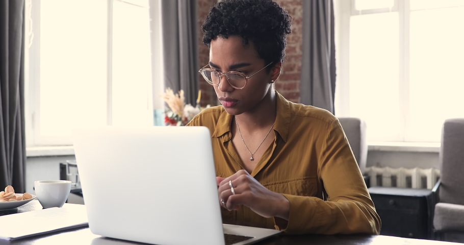 Concentrated American gen z female in eyewear work on laptop from home office fill in electronic form online browse web search data. Young lady prepare document at corporate network on distance Royalty-Free Stock Footage #1089117355