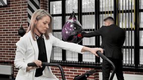 Couple of businessmen, man and woman, play sports on an exercise bike and a boxing ring in suits. - Powered by Shutterstock - Get 15% off with code: PIKWIZARD15