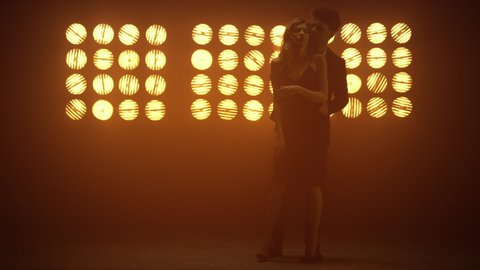 Hot man dancing behind hugging attractive woman in nightclub. Sensual guy touching girl affectionately in soft illuminate. Young lovers embracing in intimacy dance standing near bright club lamps.