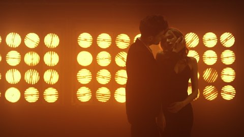 Two amorous lovers embracing intimately in night club lights. Handsome boyfriend dancing sexually with hot girlfriend in studio. Passionate couple enjoying flirting in spotlights. Nightlife concept.