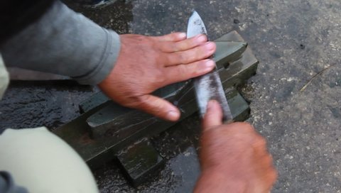 sharpening a manual knife with a whetstone, so that a sharp knife weapon for slicing and stabbing, holding a sword.