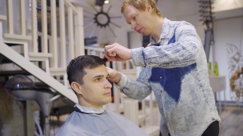 the hairdresser makes a haircut for a brunette man with a hair clipper in a barbershop. professional services. beauty salon for men. cosmetics and products for scalp and hair care.