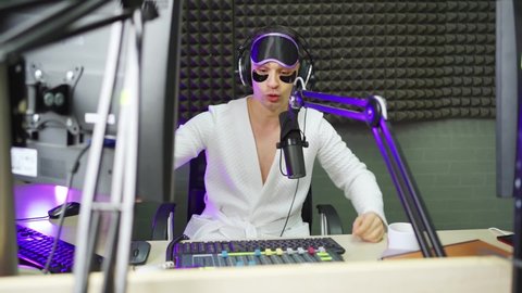 A funny radio dj in a sleep mask, bathrobe and cosmetic patches under the eyes on the broadcast in a radio studio. remote work and clothing for it. comfort and cosmetics for men.