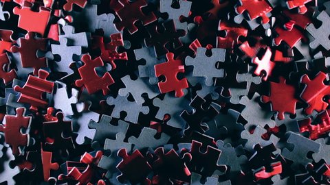 Background of Colored Puzzle Pieces that Slowly Rotating Clockwise - Top View. Texture of Incomplete Red and Grey Jigsaw Puzzle with Low Key Light - Right Rotation