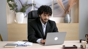Video portrait of young adult handsome joyful confident successful Indian businessman, ceo or manager with beard, in business attire, sitting at his desk in the office with a friendly smile