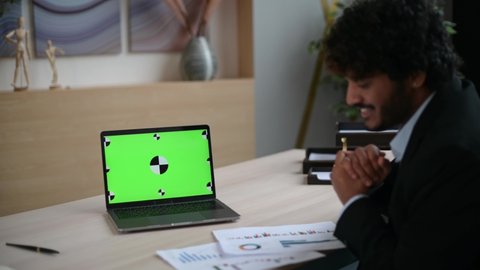 Green chromatic screen on a laptop. Online business briefing. Indian successful businessman having virtual online meeting with diverse multinational colleagues via video call using laptop