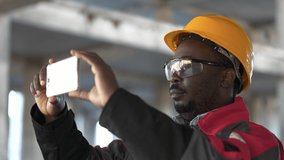 African american builder records videos on his smartphone. Worker at construction site filming a video