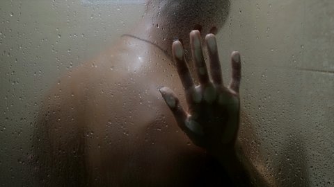 couple kissing in the shower. the male back is visible out of focus. a woman's hand slides on the glass with drops