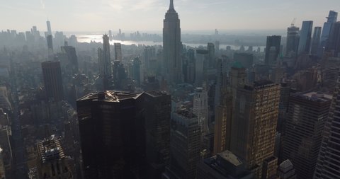 High angle view of buildings in midtown. Tilt up reveal of majestic office tower. Hazy view of Empire State Building against sun. Manhattan, New York City, USA in 2021
