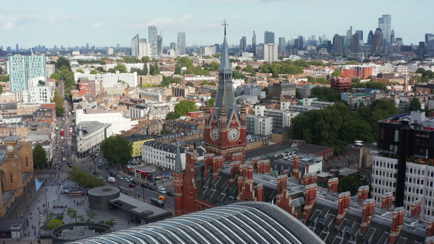 Orbit shot around clock tower at old brick building of St Pancras train station. Aerial panoramic view of city with tall skyscrapers in distance. London, UK Royalty-Free Stock Footage #1089123763
