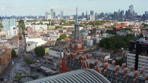 Orbit shot around clock tower at old brick building of St Pancras train station. Aerial panoramic view of city with tall skyscrapers in distance. London, UK