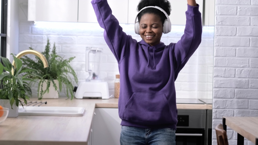 African american black handsome woman dancing with headphones enjoy life listening favourite music in kitchen at home.