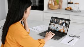 Remote video communication.Asian girl, freelancer, student or manager, working or studying remotely, sit at home in the kitchen, communicating with group of employees via video conference using laptop