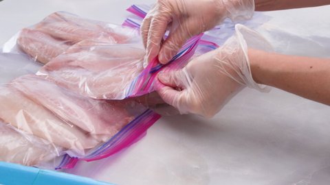 Fresh raw fish fillet in zip lock bags. Tilapia fillet on light marble background, close up. Woman hands put fillet in zip lock bags for freezing