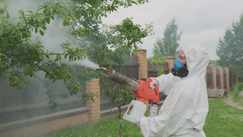 Farmer agronomist in protective suit and respirator treats fruit trees from pests and diseases using thermal spray spraying smoke with organic pesticides.