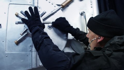 Close up of a bank robber cracking a safe. The safecracker uses a stethoscope to crack the vault security lock