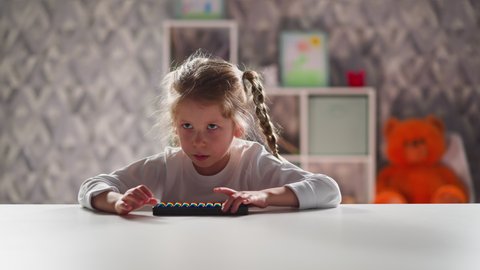 Smart little girl student with toy abacus does sums sitting at white table during mental mathematics lesson against Teddy bear closeup slow motion