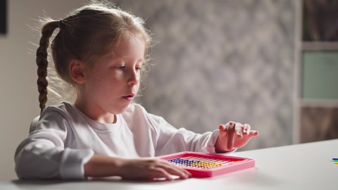 Pretty little girl preschooler learns to count by colorful toy abacus and talks at mental arithmetics lesson at home closeup slow motion