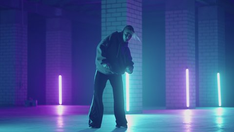 A steel woman dances hip-hop freestyle in a modern style in a hall with neon light in purple blue colors. Female Professional Hip Hop Dancer