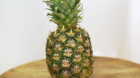 Ripe Whole Pineapple, Closeup. Isolated Background of Whole Pineapple, Tropical Fruit, Rotates on a Wooden Dish on a White Background. Healthy Vegan Food and Pineapple Diet.
