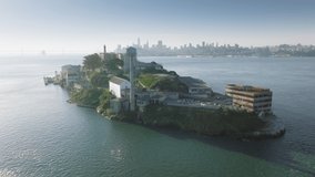 Aerial view of small picturesque island surrounded by calm sea waters with a cityscape behind. Spectacular view of the city of San Francisco as seen from the Alcatraz landmark. High quality 4k footage