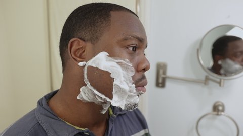 personal hygiene, African American or black man at home in bathroom using razor blade to shave beard as a barber would