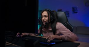 Smiling professional gamer pretty young girl wearing headset playing online video games talking joking with friends team members colorful neon led purple lights in room.