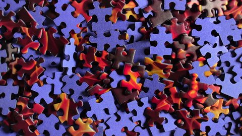 Background of Colored Puzzle Pieces that Slowly Rotating Counterclockwise - Top View. Texture of Incomplete Red and Blue Jigsaw Puzzle - Left Rotation
