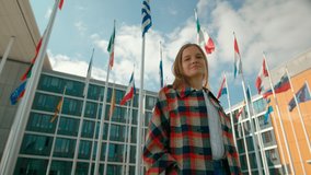 Portrait of Young Woman with Waving Flags of European Union Countries Outside of European Parliament administrative office in Luxembourg City. Politics, Migration and Citizenship concept. 4K shot - Powered by Shutterstock - Get 15% off with code: PIKWIZARD15