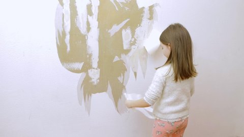 a little girl removes old wallpaper from the wall and prepares to make repairs in the room