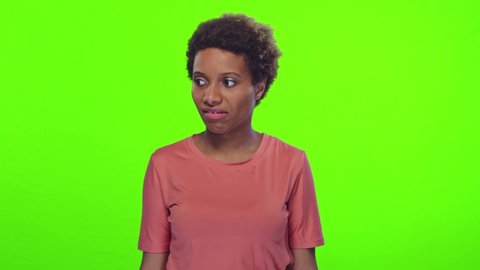 Young funny short haired African American woman with bulging eyes feels bad odor from something closes nose and waves hand to disperse stench is disgusted stands in studio on green background