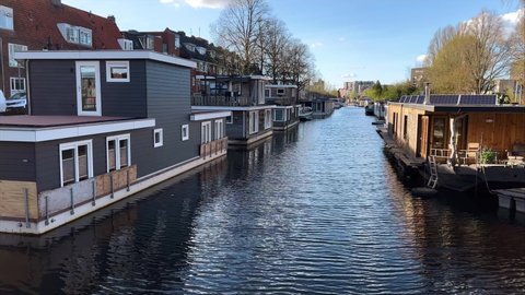 GRONINGEN, NETHERLANDS - 10. APRIL 2022: Steady shot of beautiful houseboats in city canal of Groningen with calm water.