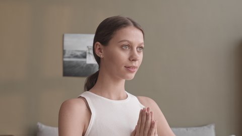 Tilt-up slowmo shot of concentrated young Caucasian pregnant woman meditating in standing position with praying hands at home, inhaling and exhaling deeply